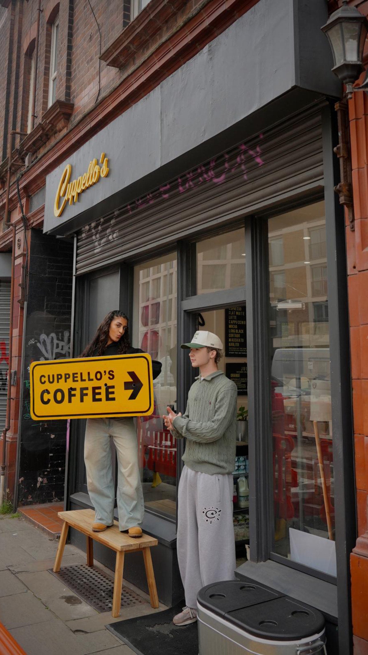 Two people standing outside a coffee shop with a 'Cupello's Coffee' sign.